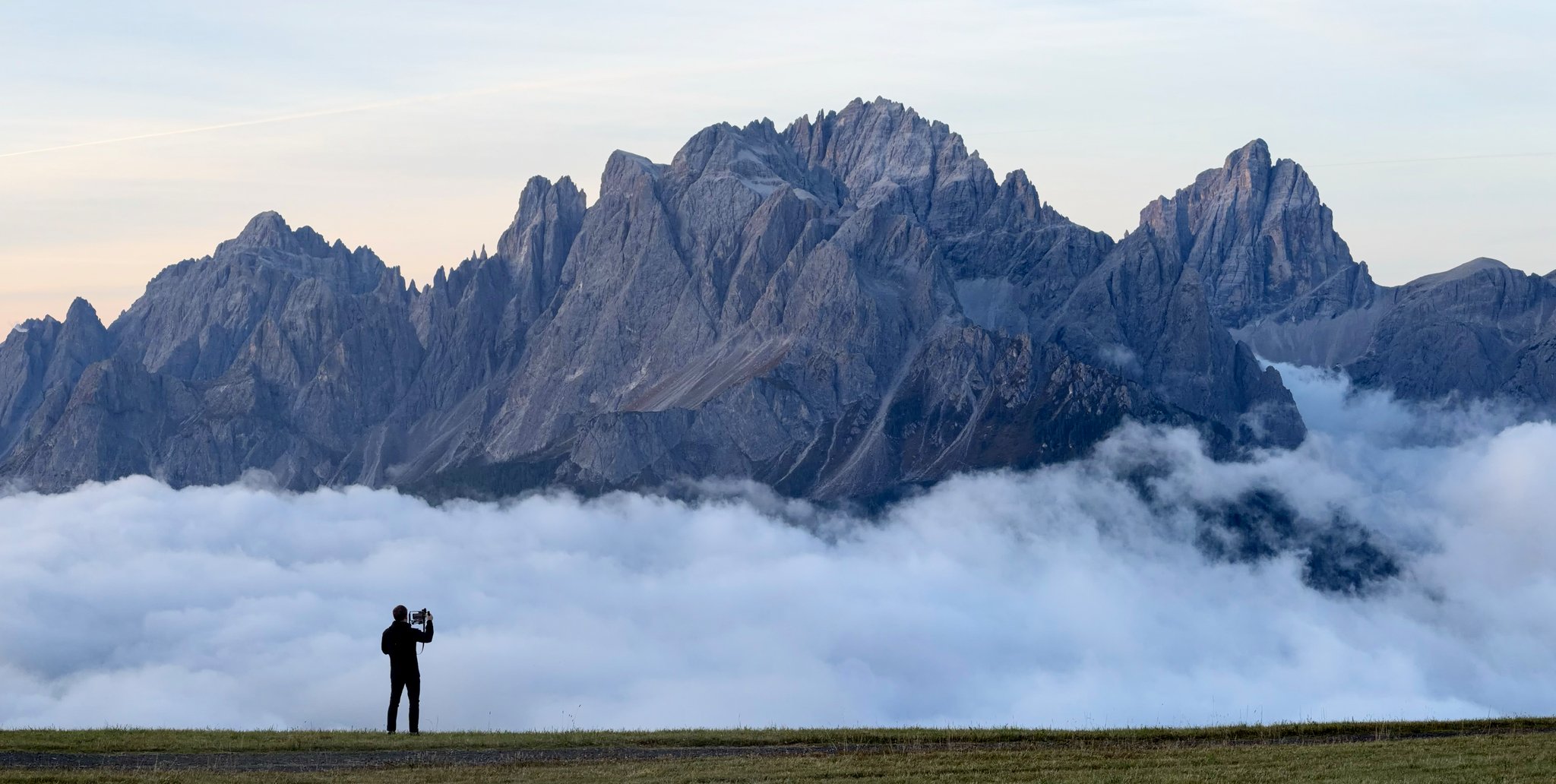 A lone figure photographing the Dolomite peaks above a sea of cloud at dusk